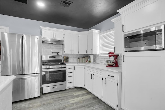 kitchen with visible vents, light wood-style flooring, stainless steel appliances, light countertops, and under cabinet range hood