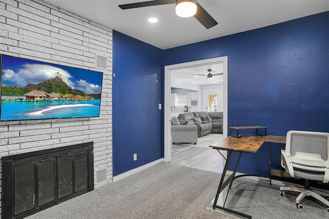 carpeted office featuring a brick fireplace, baseboards, and a ceiling fan