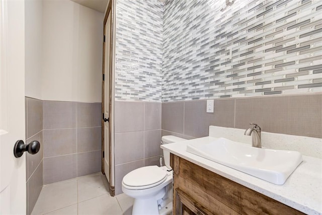 half bath with toilet, a wainscoted wall, tile patterned flooring, vanity, and tile walls