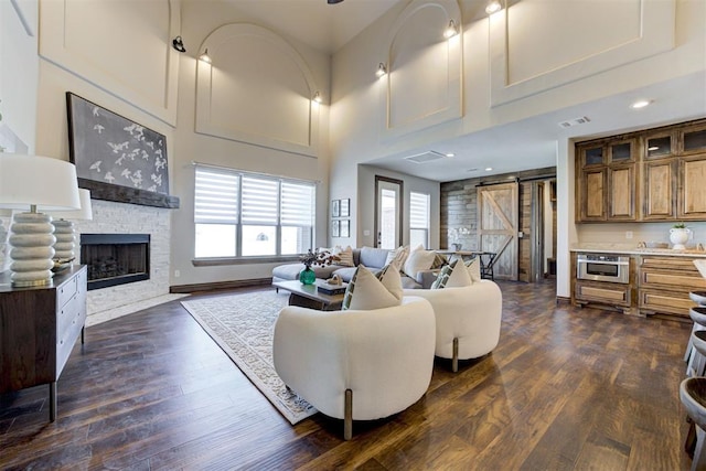 living room featuring dark wood finished floors, a stone fireplace, a towering ceiling, and a barn door