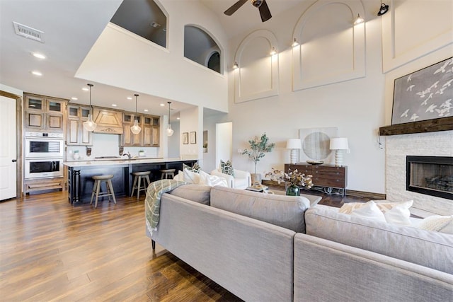 living room featuring visible vents, a ceiling fan, dark wood-type flooring, a high ceiling, and a fireplace