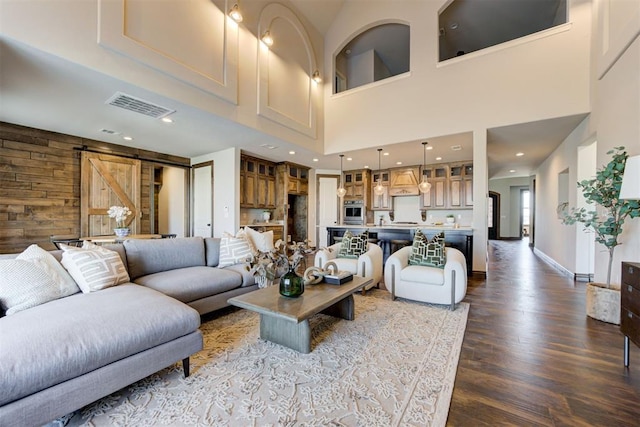 living area featuring a barn door, recessed lighting, wooden walls, dark wood-style flooring, and visible vents