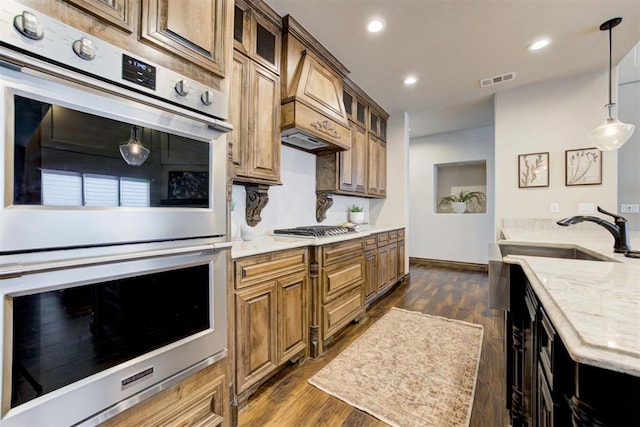 kitchen with dark wood-style floors, stainless steel appliances, visible vents, glass insert cabinets, and a sink