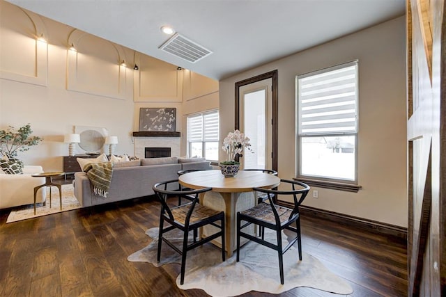 dining room with baseboards, visible vents, dark wood finished floors, and a fireplace