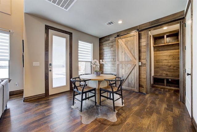 dining space with a barn door, dark wood-type flooring, wood walls, and visible vents