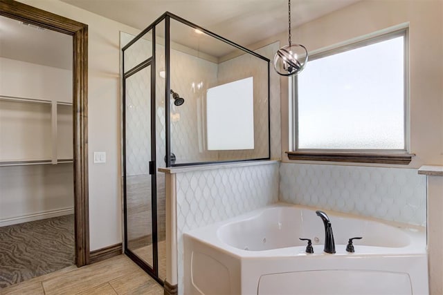 full bathroom featuring a spacious closet, a tub with jets, a shower stall, and wood tiled floor