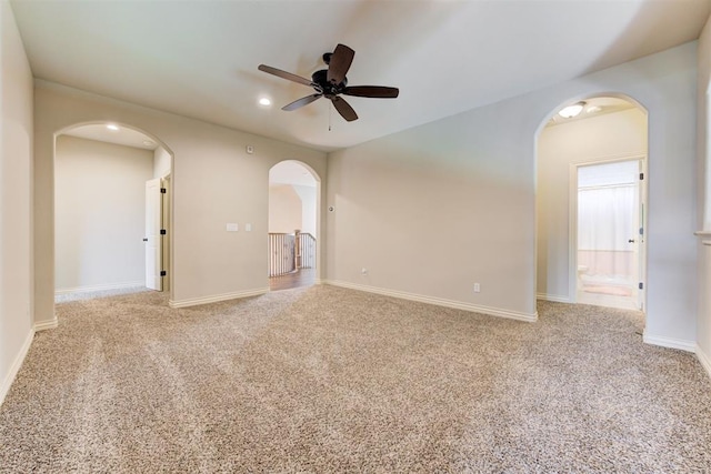 carpeted spare room with a ceiling fan, arched walkways, and baseboards