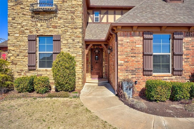 entrance to property featuring brick siding, stone siding, and roof with shingles