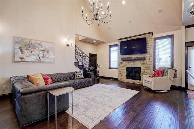 living room with dark wood-style floors, a high ceiling, a stone fireplace, baseboards, and stairs