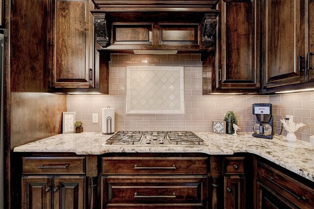 kitchen with stainless steel gas stovetop, dark brown cabinets, backsplash, and light stone counters