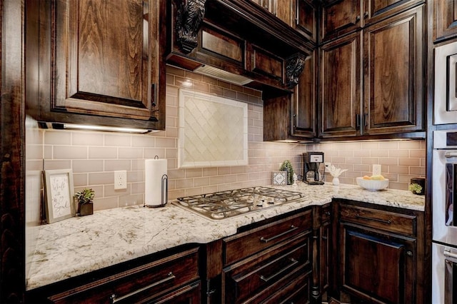 kitchen with dark brown cabinetry, decorative backsplash, appliances with stainless steel finishes, and light stone countertops