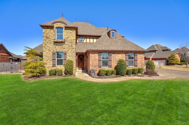 view of front of house with stone siding, fence, a front yard, a shingled roof, and brick siding