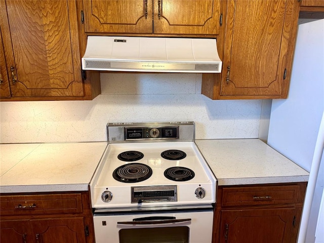 kitchen featuring light countertops, electric range, brown cabinetry, and under cabinet range hood