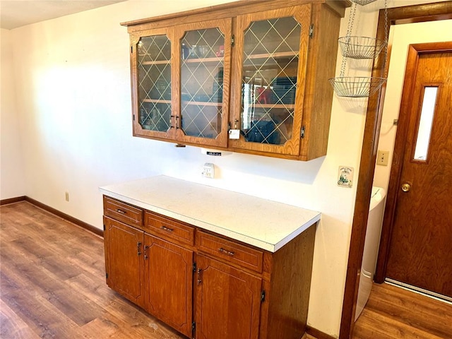 kitchen with light countertops, brown cabinetry, wood finished floors, and baseboards