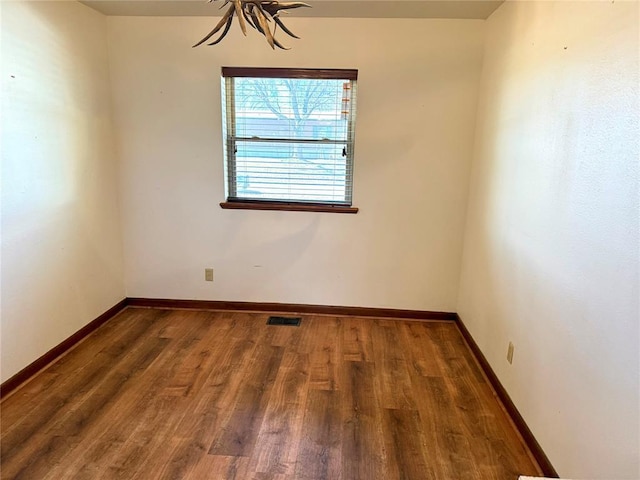 spare room featuring wood finished floors, visible vents, and baseboards