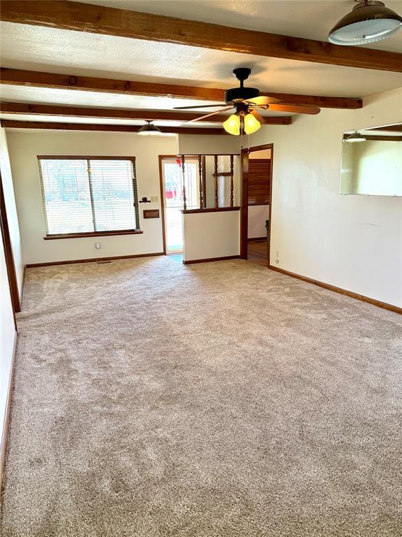 spare room with ceiling fan, a textured ceiling, light carpet, baseboards, and beamed ceiling