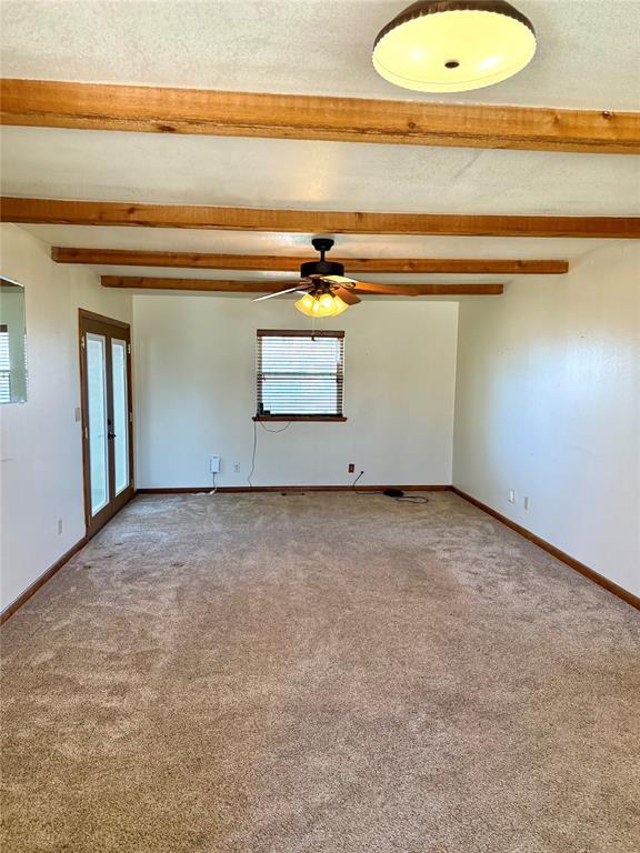 carpeted spare room with a textured ceiling, baseboards, and beam ceiling