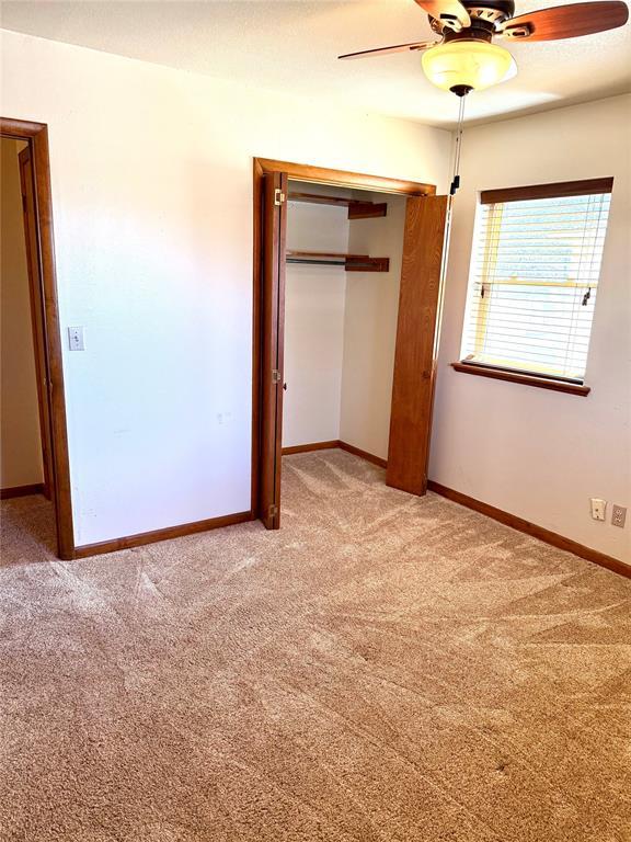 unfurnished bedroom featuring a ceiling fan, baseboards, a closet, and light colored carpet