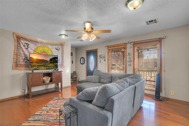 living room featuring visible vents, a textured ceiling, a ceiling fan, and wood finished floors