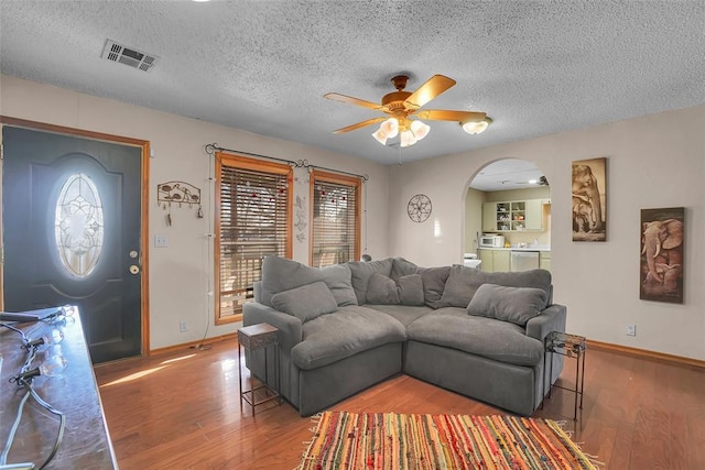 living room featuring a ceiling fan, wood finished floors, visible vents, and arched walkways