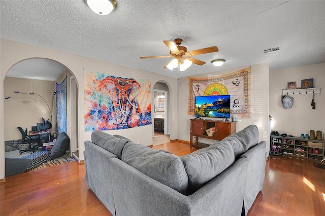 living area featuring a textured ceiling, wood finished floors, visible vents, and arched walkways