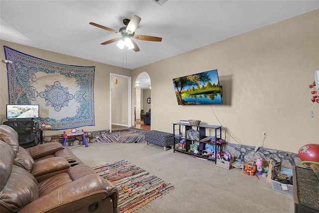 living area featuring arched walkways, carpet floors, and ceiling fan