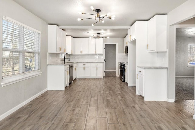 kitchen with stainless steel appliances, tasteful backsplash, a sink, a chandelier, and light wood-type flooring