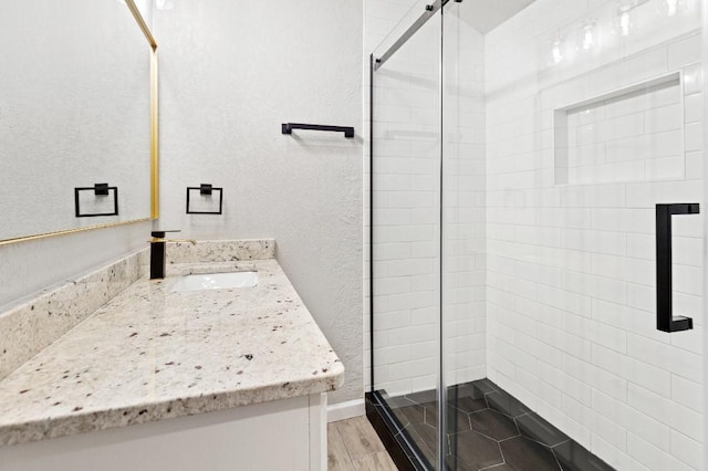 full bath with a textured wall, a stall shower, wood finished floors, and vanity