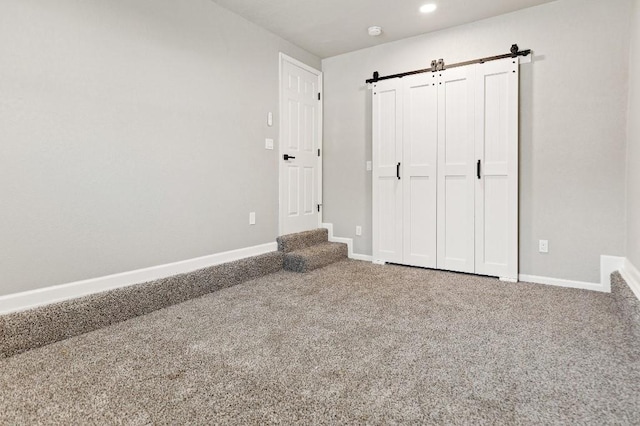 unfurnished bedroom with carpet, baseboards, and a barn door