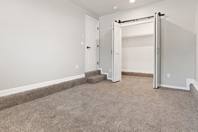 unfurnished bedroom with a barn door, baseboards, a spacious closet, a closet, and carpet