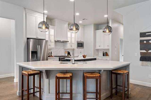 kitchen with stainless steel appliances, dark wood finished floors, white cabinetry, a sink, and a large island with sink