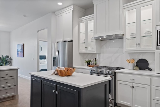 kitchen with white cabinets, light countertops, stainless steel appliances, a kitchen island, and glass insert cabinets