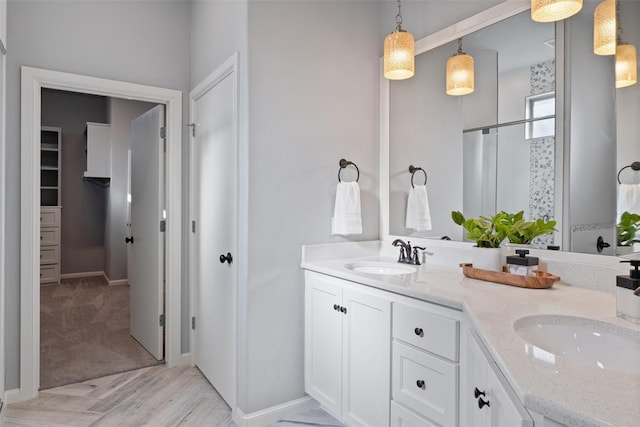 bathroom with baseboards, a shower with shower door, a sink, and double vanity