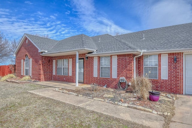 ranch-style home featuring a shingled roof, brick siding, and fence