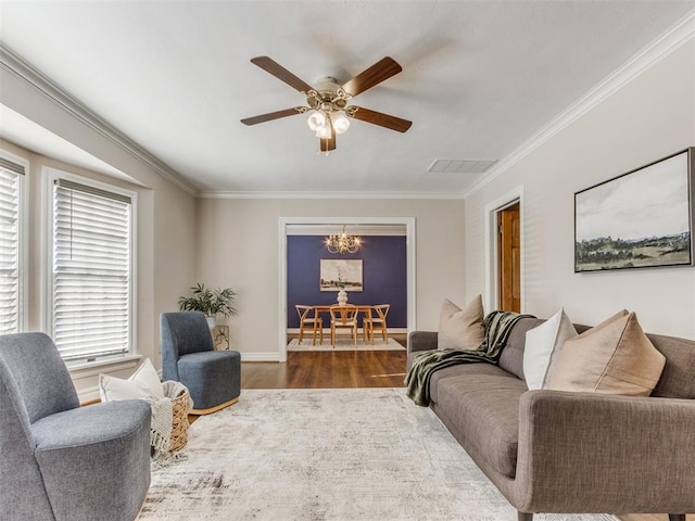 living area featuring baseboards, visible vents, ornamental molding, wood finished floors, and ceiling fan with notable chandelier
