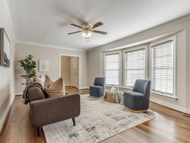 living area with visible vents, ornamental molding, a ceiling fan, wood finished floors, and baseboards