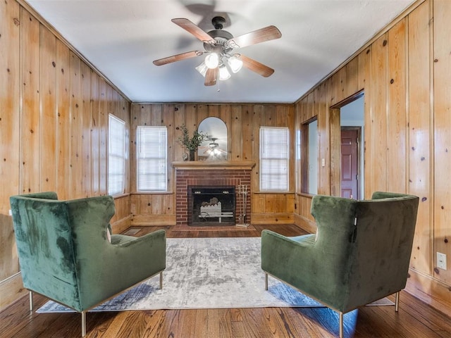 living area featuring ceiling fan, a brick fireplace, wood walls, and wood finished floors