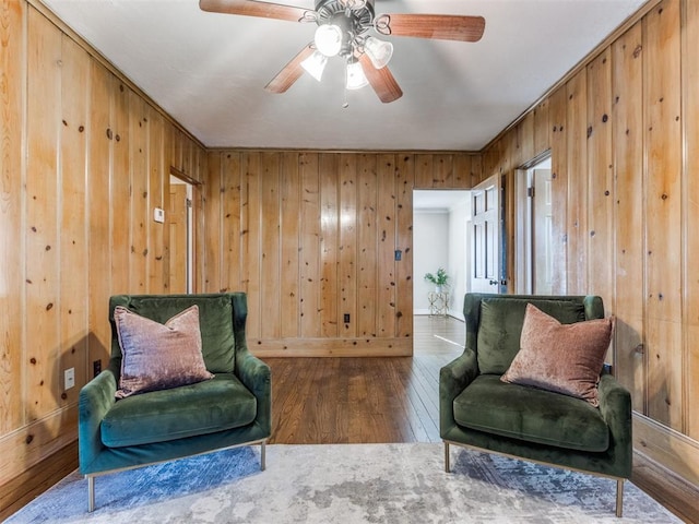 living area with a ceiling fan, wood walls, and hardwood / wood-style flooring