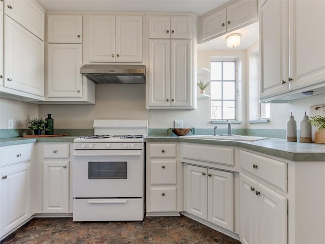 kitchen featuring white gas stove, stone finish flooring, white cabinetry, a sink, and under cabinet range hood