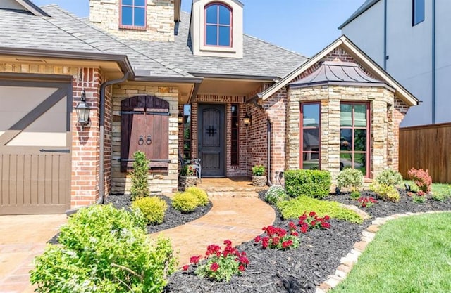 doorway to property with a garage, brick siding, fence, stone siding, and roof with shingles