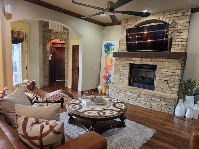 living area with ornamental molding, arched walkways, a stone fireplace, and wood finished floors