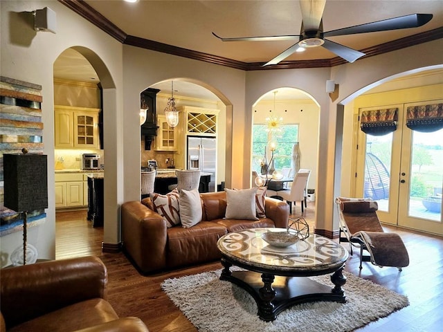 living area with ornamental molding, wood finished floors, and ceiling fan with notable chandelier