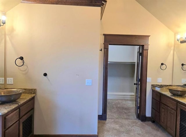 bathroom with lofted ceiling, two vanities, a sink, and tile patterned floors