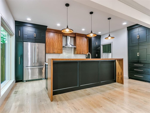 kitchen with light wood finished floors, a sink, wall chimney exhaust hood, high quality fridge, and tasteful backsplash