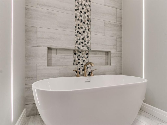 bathroom featuring marble finish floor, baseboards, and a freestanding bath