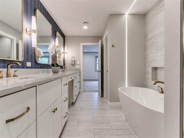 bathroom with double vanity, baseboards, visible vents, a freestanding tub, and a sink