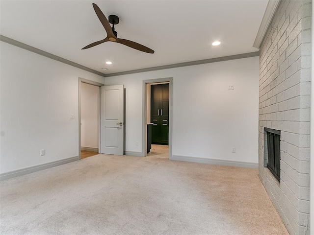 unfurnished living room with light colored carpet, a fireplace, a ceiling fan, baseboards, and crown molding