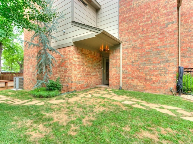 entrance to property with central air condition unit, fence, and a yard