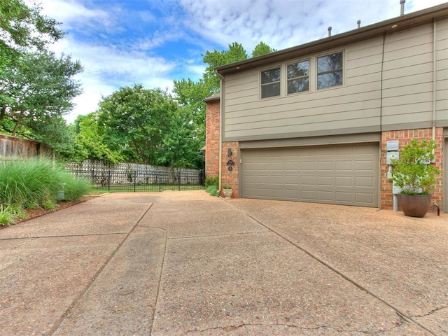 view of home's exterior featuring driveway, brick siding, an attached garage, and fence