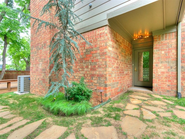 view of exterior entry featuring brick siding, cooling unit, and fence